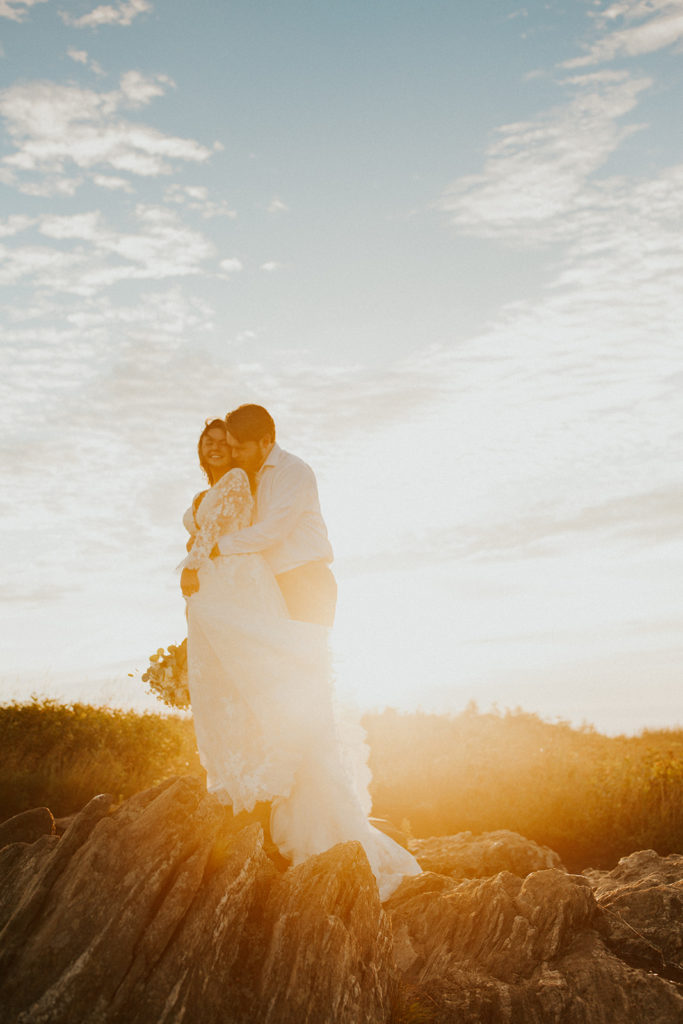 Husband hugging his wife from behind on top of a mountain during sunrise