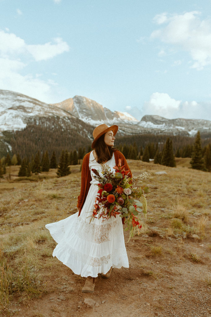 a woman in wedding attire holding a bouquet gazes off to the right with mountains in the background