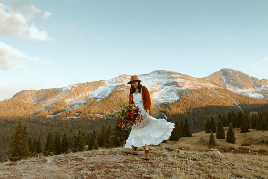 a woman in a wedding dress holds a bouquet and dances with mountains in the background