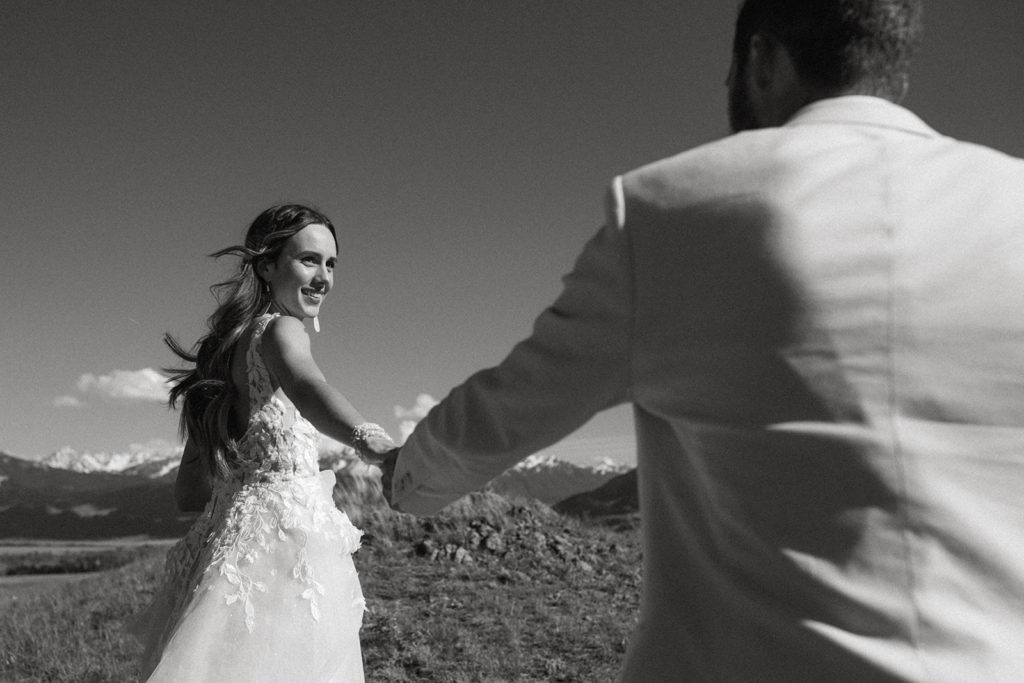 Black and white photo of a bride looking at the groom with their hands held out toward each other and the groom facing a way from the camera during their elopement in Montana.