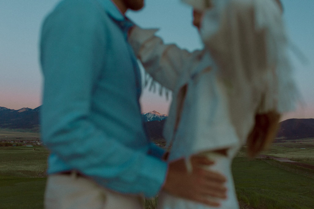 Up close photo of a blurry bride and groom embracing with mountains in focus in the background during their Montana elopement.