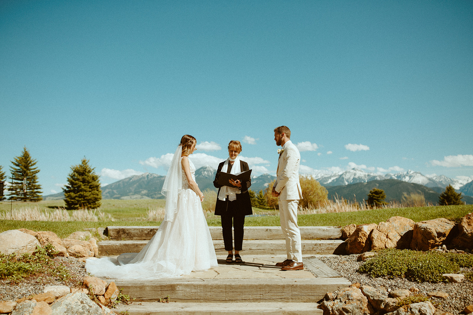 An officiant marries a bride and groom with a mountain landscape in the background.
