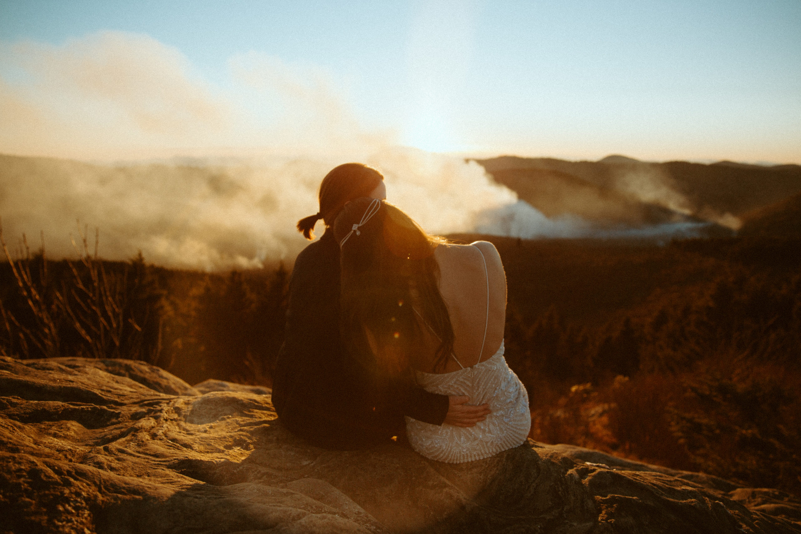 Two brides during a sunset elopement looking off into the distance at the mountains, fog, and beautiful sky.