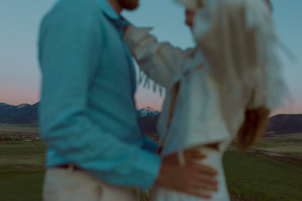A bride and groom begin to embrace during their sunset elopement. A large field and mountains can be seen in the background.