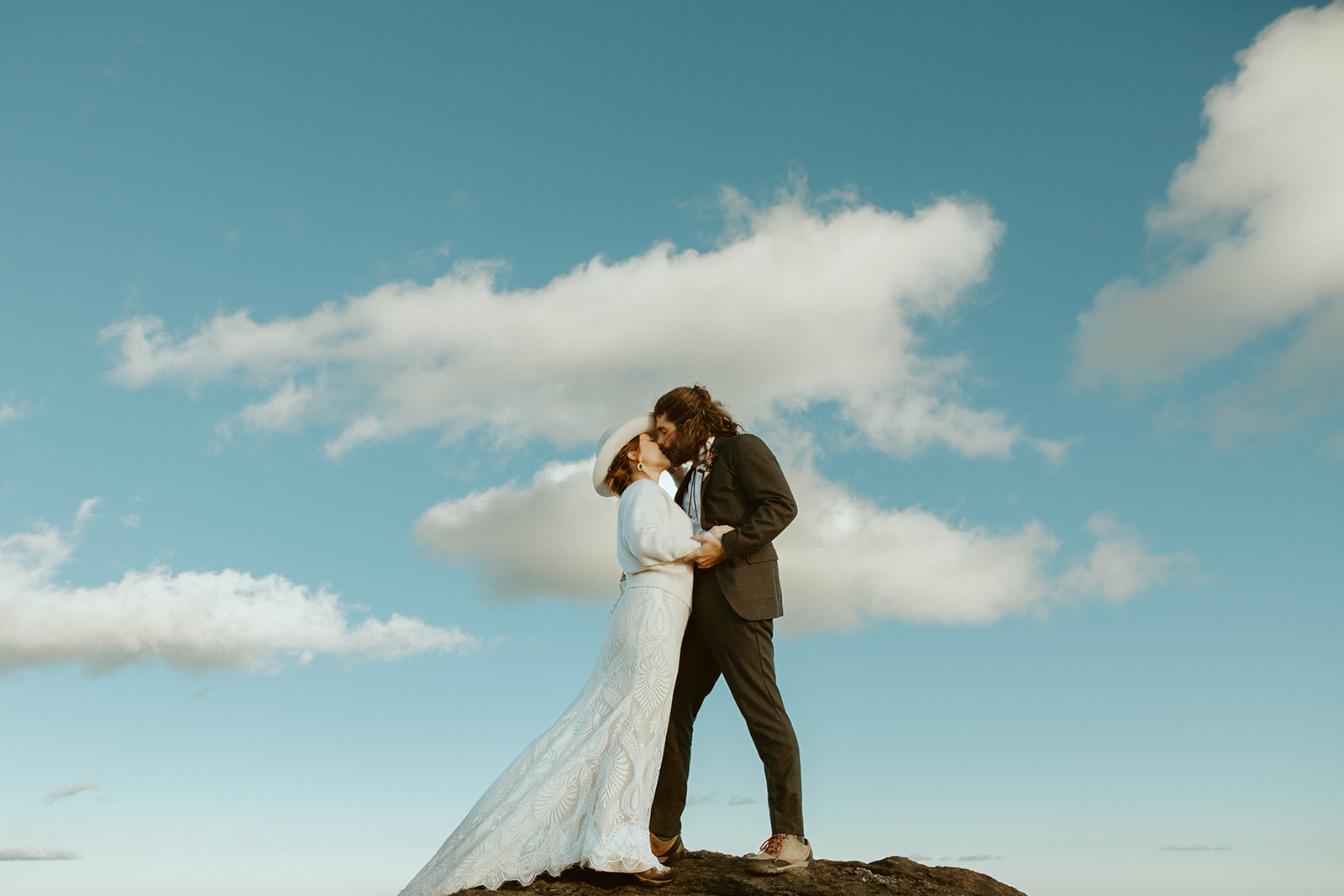 A bride and groom embrace and kiss on top of a mountain during their winter elopement.