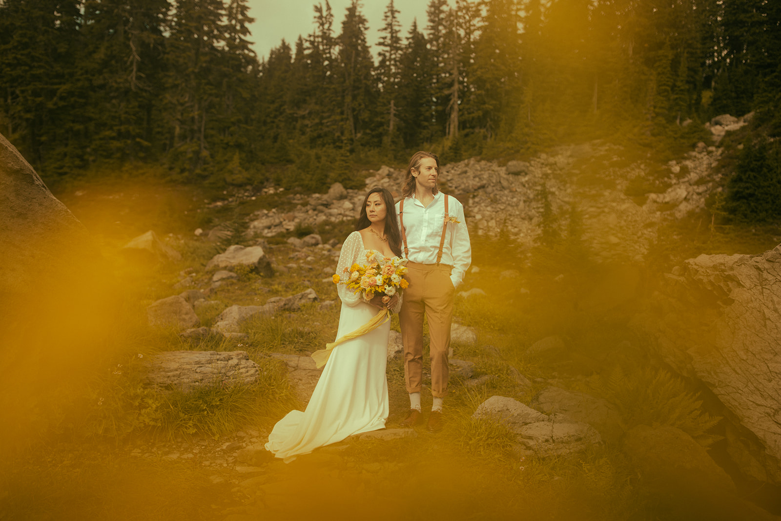 A bride and groom gaze out into the open with a rocky, forest landscape behind them during their spring elopement.